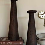 Two dark brown ceramic vases on a shelf with books and bowls in the background.