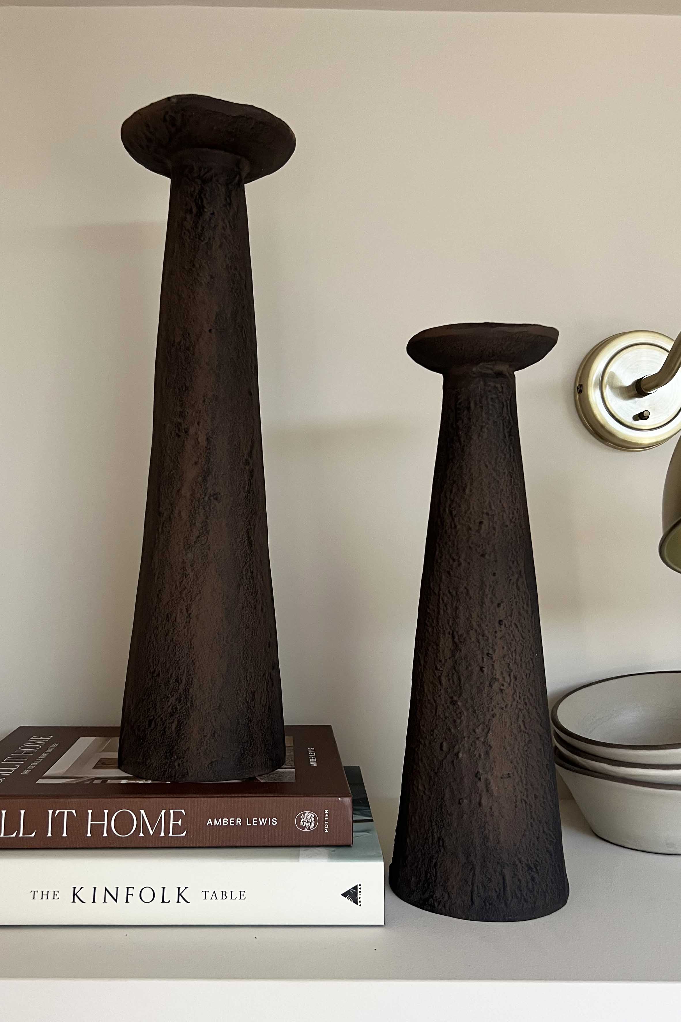 Two dark brown ceramic vases on a shelf with books and bowls in the background.