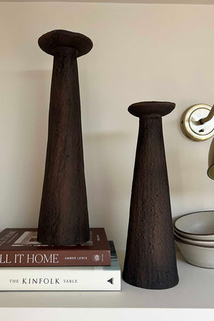 Two dark brown ceramic vases on a shelf with books and bowls in the background.