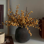 Decorative faux plant in a black vase on a shelf with books and a framed picture. Rtfact Flowers