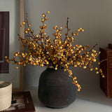 Decorative faux plant in a black vase on a shelf with books and a framed picture. Rtfact Flowers