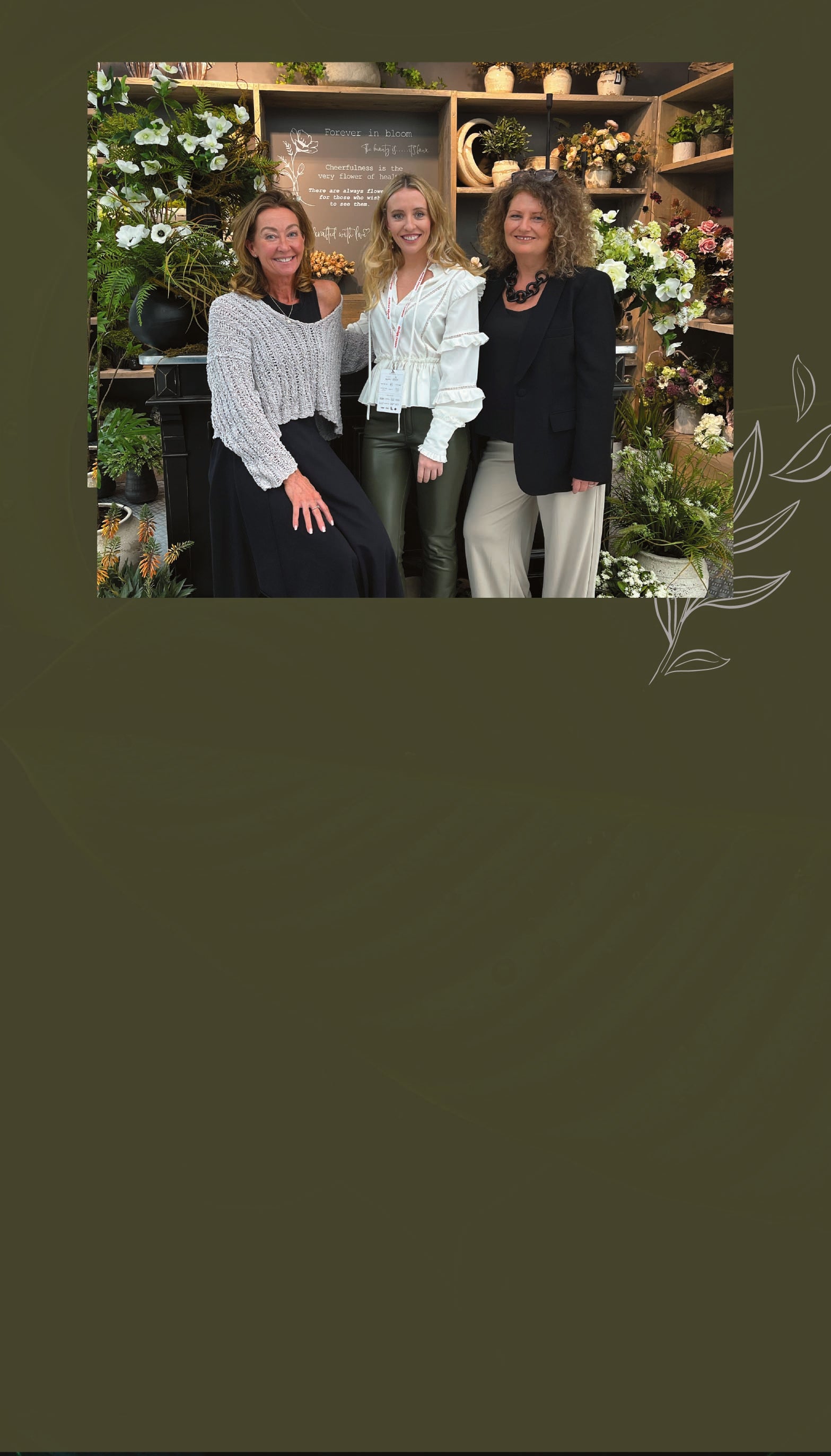 Three women posing together in a garden center setting with plants and decor.