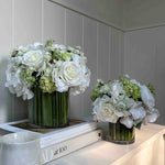 Two faux floral arrangements in glass vases on a white surface with a neutral background. Rtfact