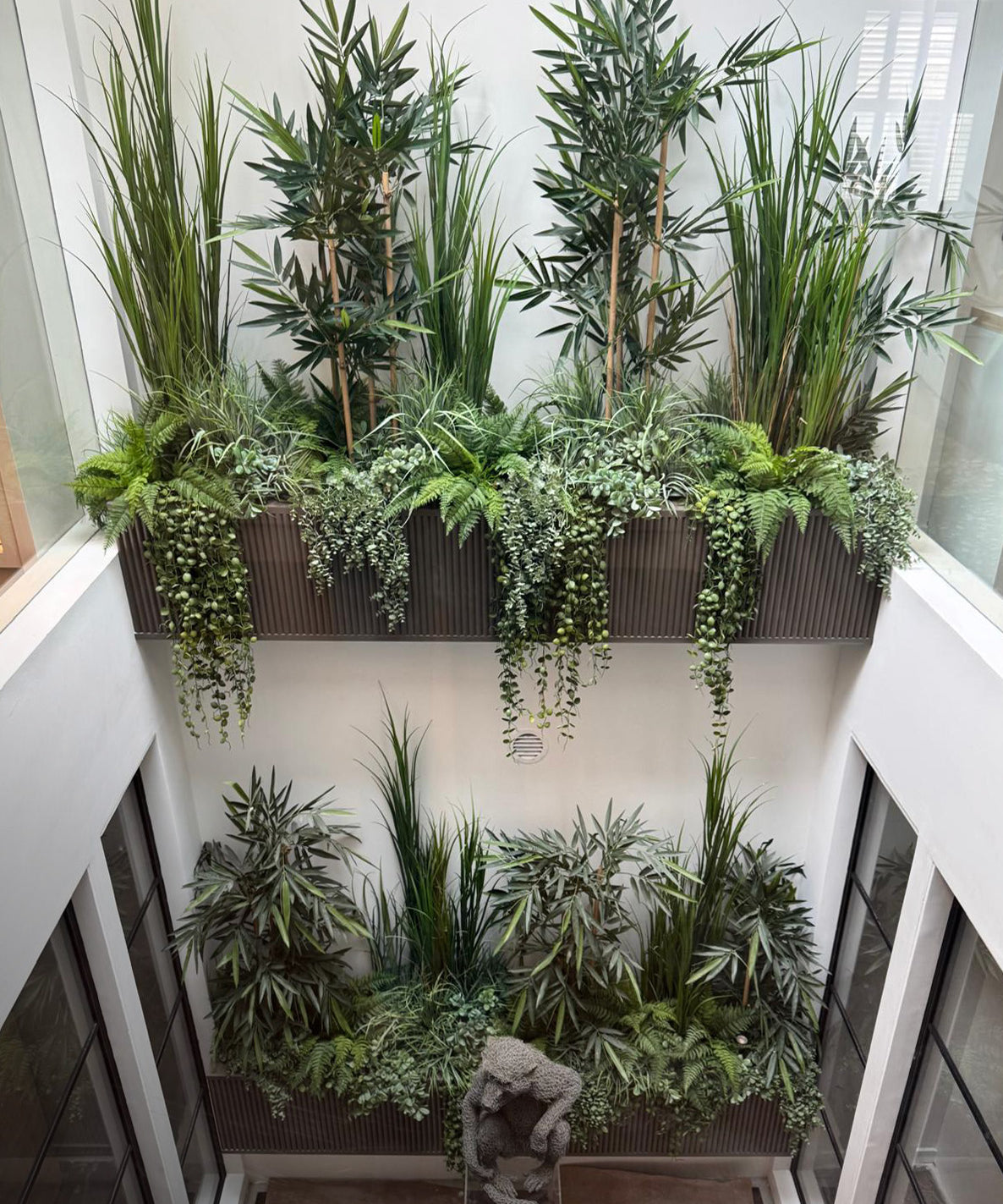 Indoor planters with various green plants on a white wall.