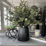 Decorative vase with faux flowers and greenery on a gray surface with a mirror background. Rtfact