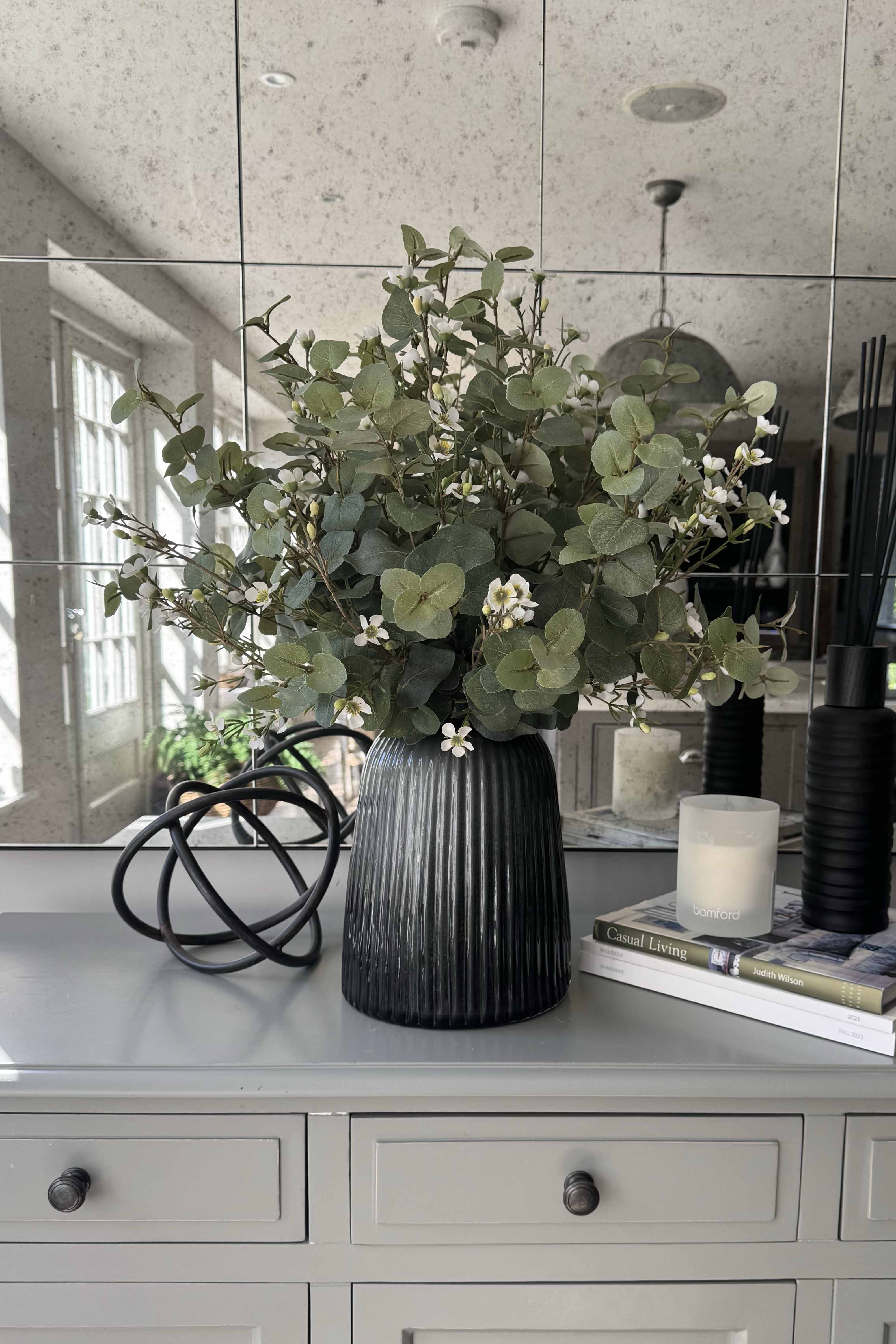 Decorative vase with faux flowers and greenery on a gray surface with a mirror background. Rtfact