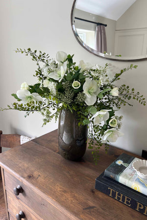 Faux Floral arrangement in a vase on a wooden dresser with a mirror above. Rtfact