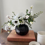 Faux white Floral arrangement in a black vase on a wooden surface with a book and small dish. Interior decor. rtfact