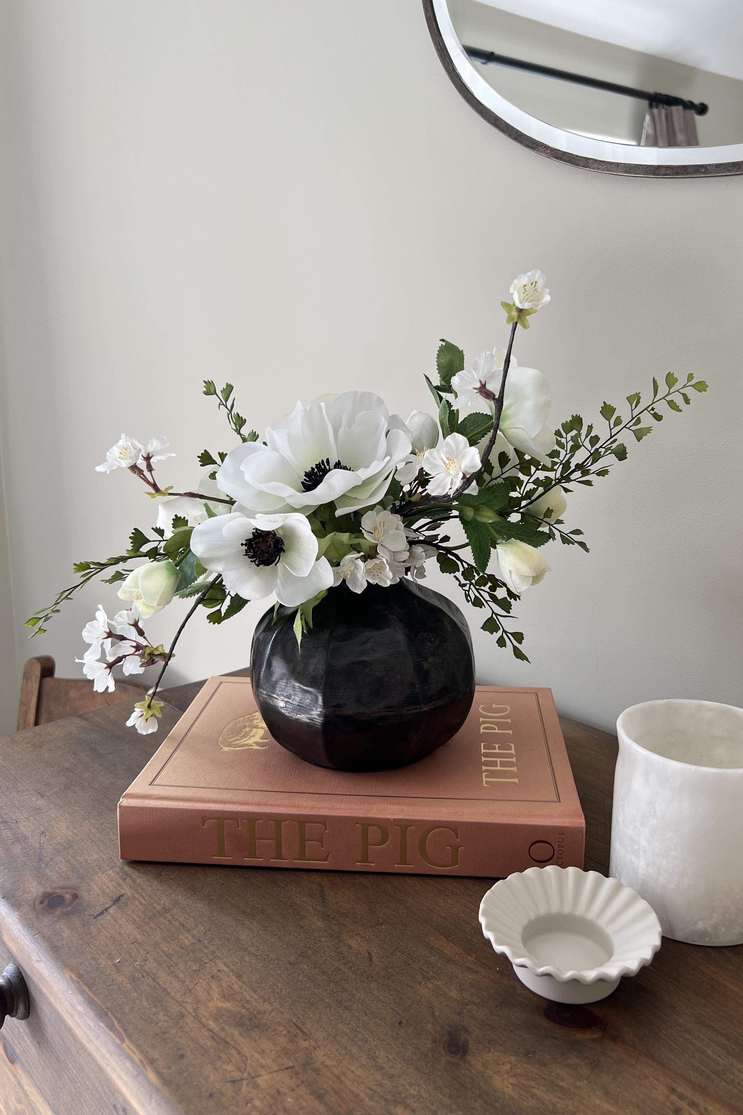 Faux white Floral arrangement in a black vase on a wooden surface with a book and small dish. Interior decor. rtfact