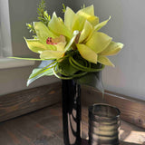 Vase with faux orchid flowers on a wooden surface next to a glass container. Rtfact 