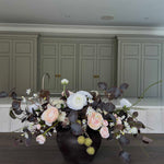 Faux Floral centrepiece arrangement in a black vase on a wooden table with green cabinets in the background