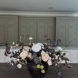 Faux Floral centrepiece arrangement in a black vase on a wooden table with green cabinets in the background