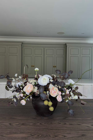 Faux Floral centrepiece arrangement in a black vase on a wooden table with green cabinets in the background