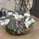 Decorative faux floral arrangement with white flowers and succulents on a wooden surface. Rtfact flowers