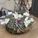 Decorative faux floral arrangement with white flowers and succulents on a wooden surface. Rtfact flowers