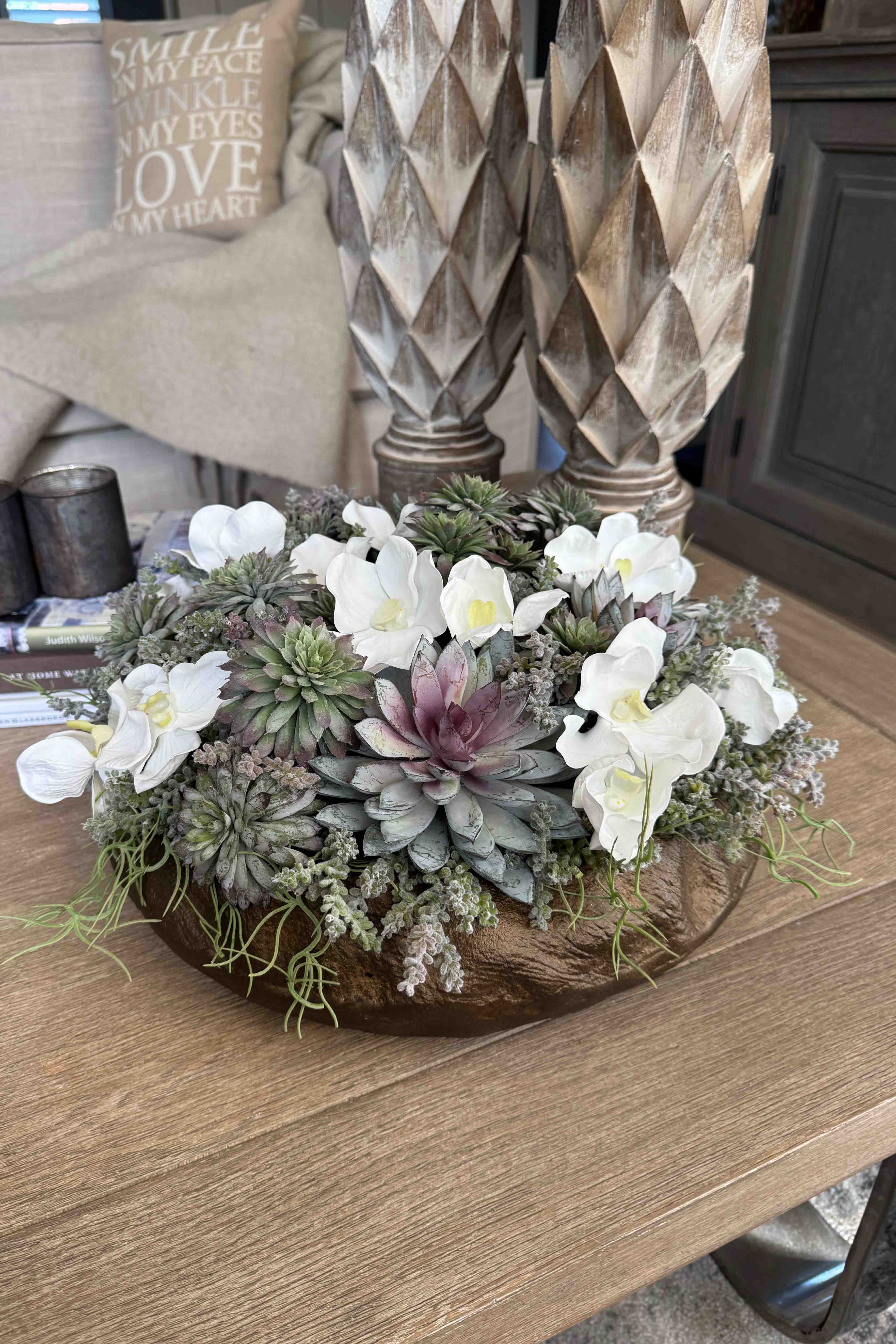 Decorative faux floral arrangement with white flowers and succulents on a wooden surface. Rtfact flowers