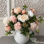 Bouquet of pink and white faux flowers in a white vase on a gray surface with decorative wall in the background. Rtfact Flowers