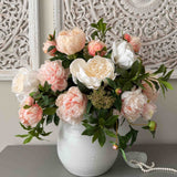 Bouquet of pink and white faux flowers in a white vase on a gray surface with decorative wall in the background. Rtfact Flowers