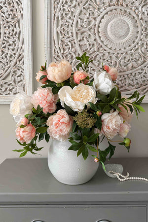 Bouquet of pink and white faux flowers in a white vase on a gray surface with decorative wall in the background. Rtfact Flowers