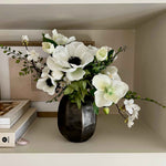 Faux Floral arrangement in a black vase on a shelf with books and decorative items.
