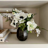 Faux Floral arrangement in a black vase on a shelf with books and decorative items.