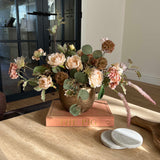 Decorative faux floral arrangement on a wooden surface with a blurred background. rtfact