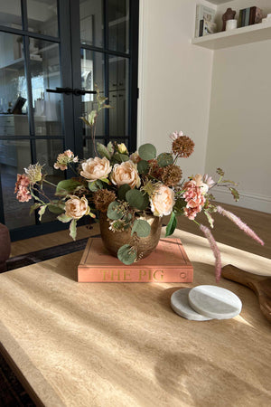 Decorative faux floral arrangement on a wooden surface with a blurred background. rtfact