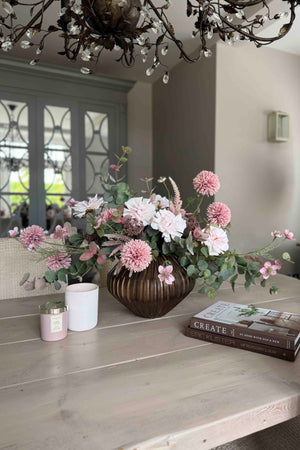 Faux floral arrangement on a wooden table with a chandelier above