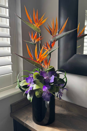 Decorative faux flower arrangement with orange and purple flowers in a black vase on a windowsill. rtfact flowers