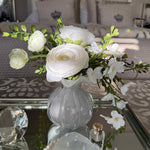 Decorative arrangement of white flowers in a clear vase on a glass table with a blurred background.
