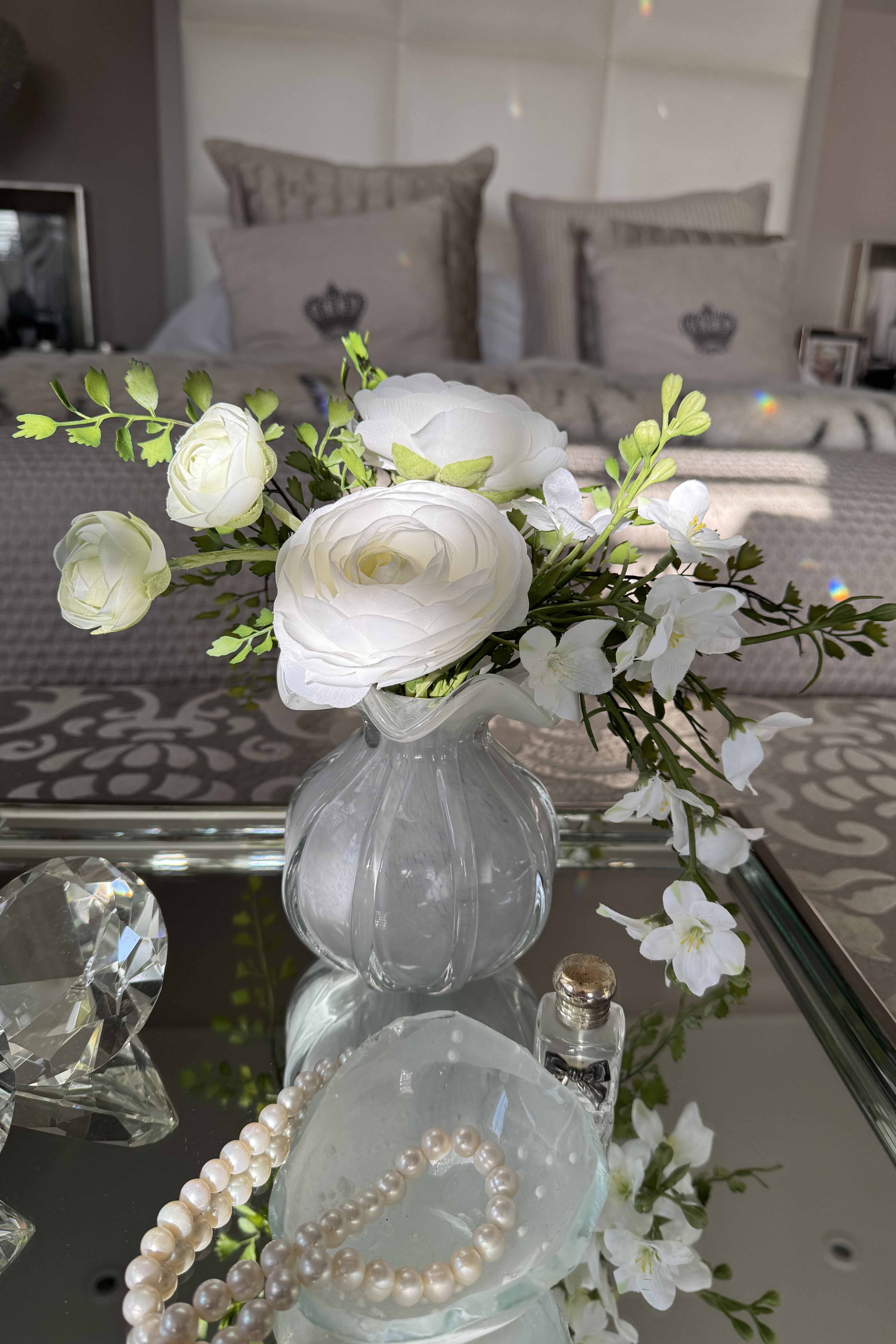 Decorative arrangement of white flowers in a clear vase on a glass table with a blurred background.