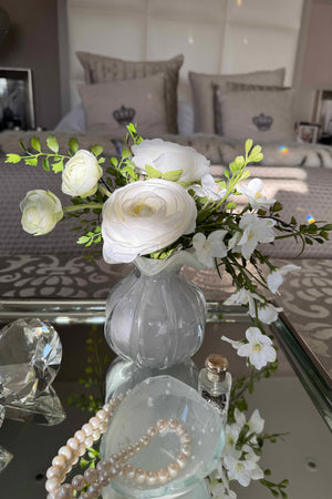 Decorative arrangement of white flowers in a clear vase on a glass table with a blurred background.