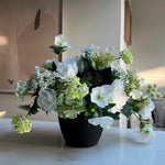 Faux floral arrangement in a pot on a white surface with a neutral background