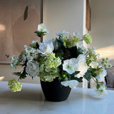Faux floral arrangement in a pot on a white surface with a neutral background