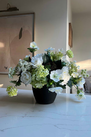 Faux floral arrangement in a pot on a white surface with a neutral background