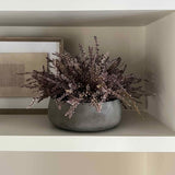 Gray vase with faux plants on a white shelf against a neutral wall