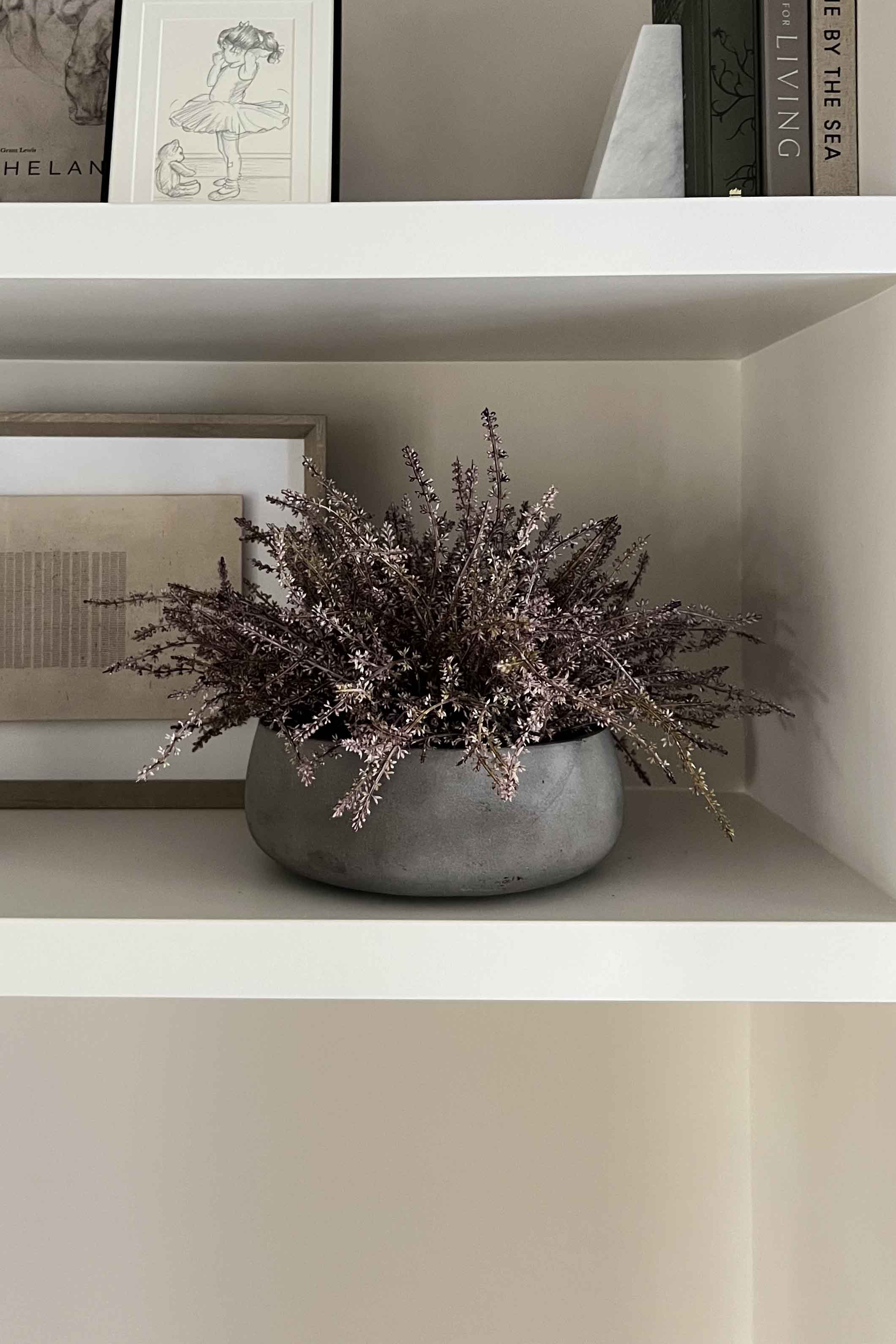 Gray vase with faux plants on a white shelf against a neutral wall