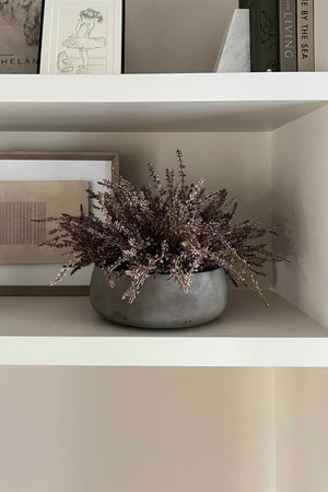 Gray vase with faux plants on a white shelf against a neutral wall