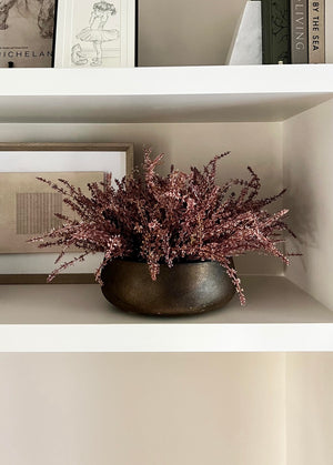 Decorative faux plant in a pot on a shelf with framed pictures in the background