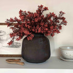 Decorative vase with artificial red branches on a shelf against a neutral wall. Rtfact