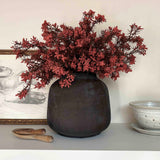 Decorative vase with artificial red branches on a shelf against a neutral wall. Rtfact