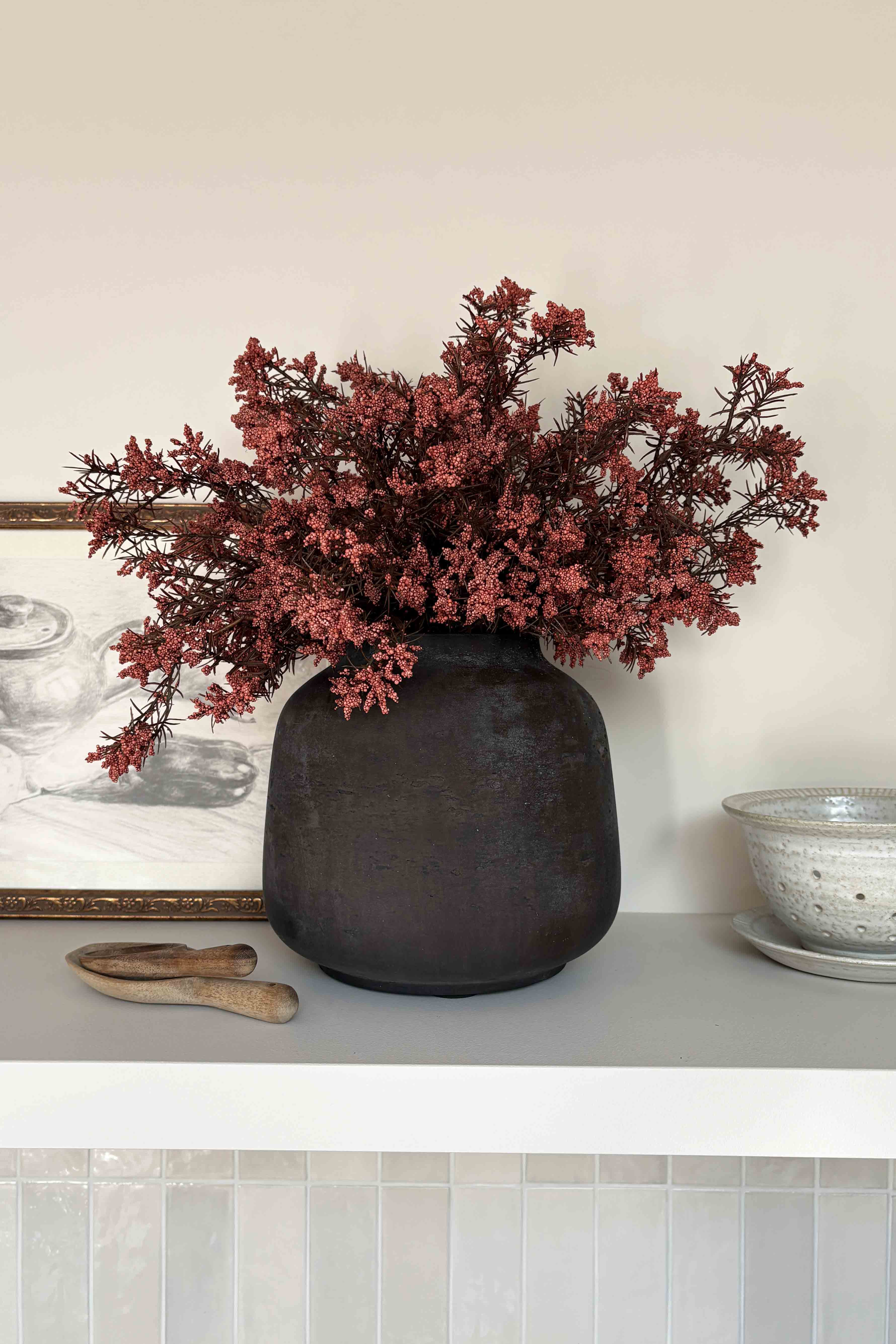 Decorative vase with artificial red branches on a shelf against a neutral wall. Rtfact