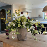 Floral arrangement in a vase on a wooden table with a kitchen in the background