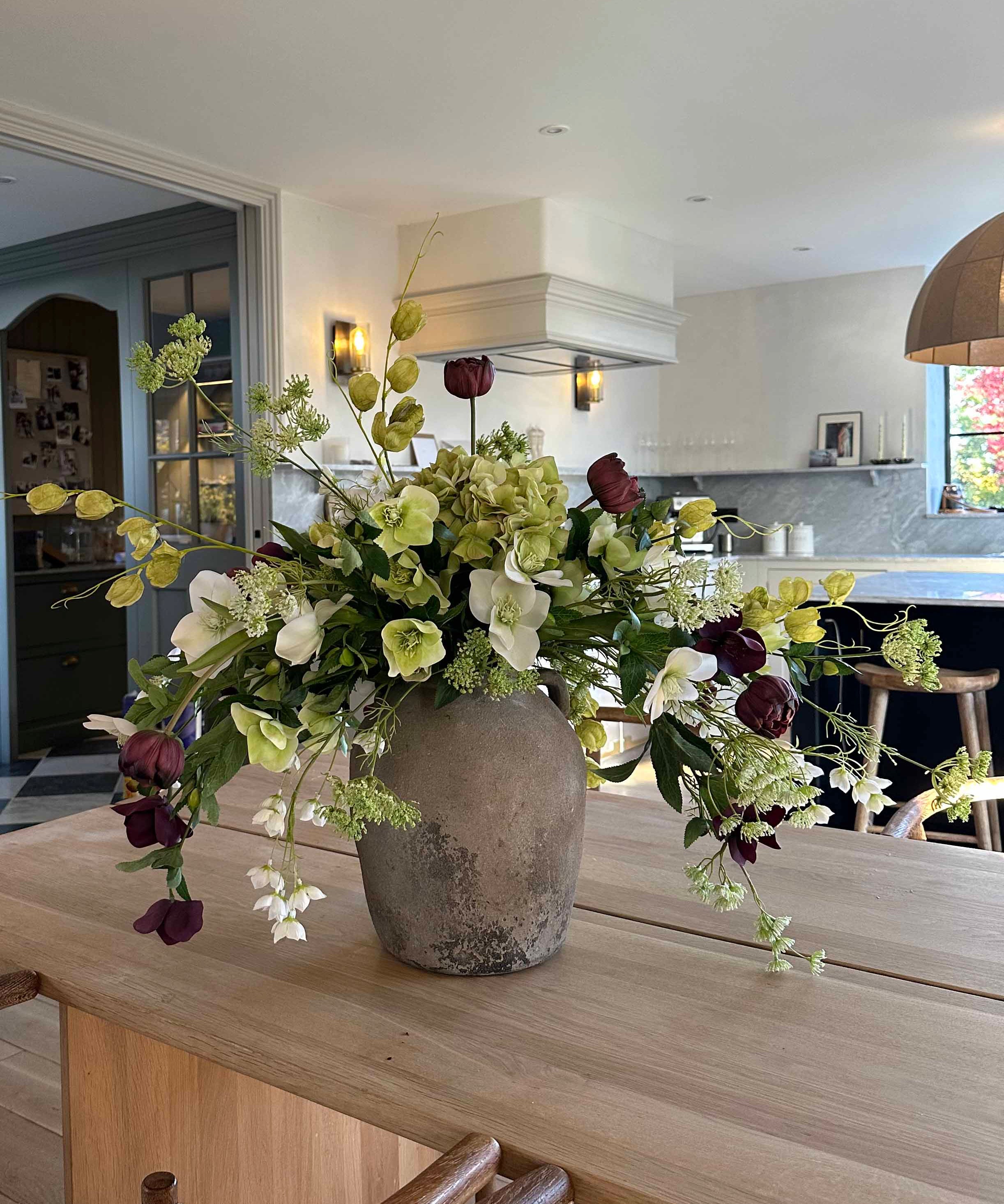Floral arrangement in a vase on a wooden table with a kitchen in the background