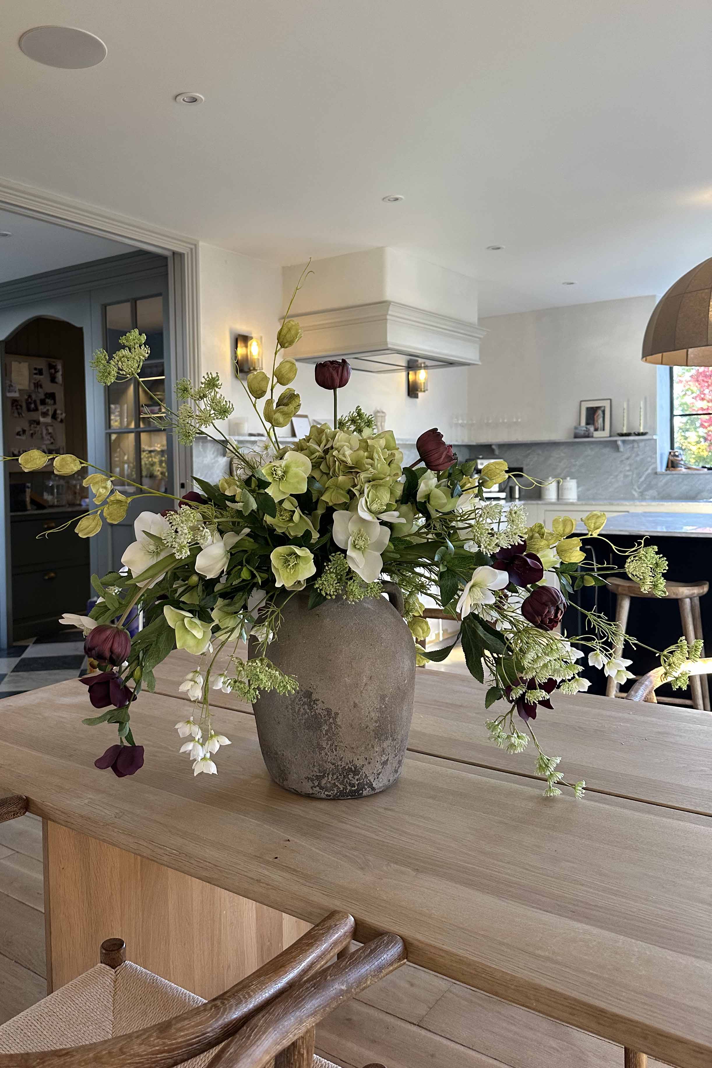 Floral arrangement in a vase on a wooden table with a kitchen in the background