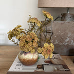 Decorative vase with flowers on a book titled 'Create' next to a lamp.