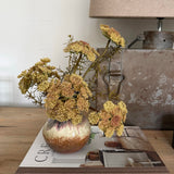 Decorative vase with flowers on a book titled 'Create' next to a lamp.