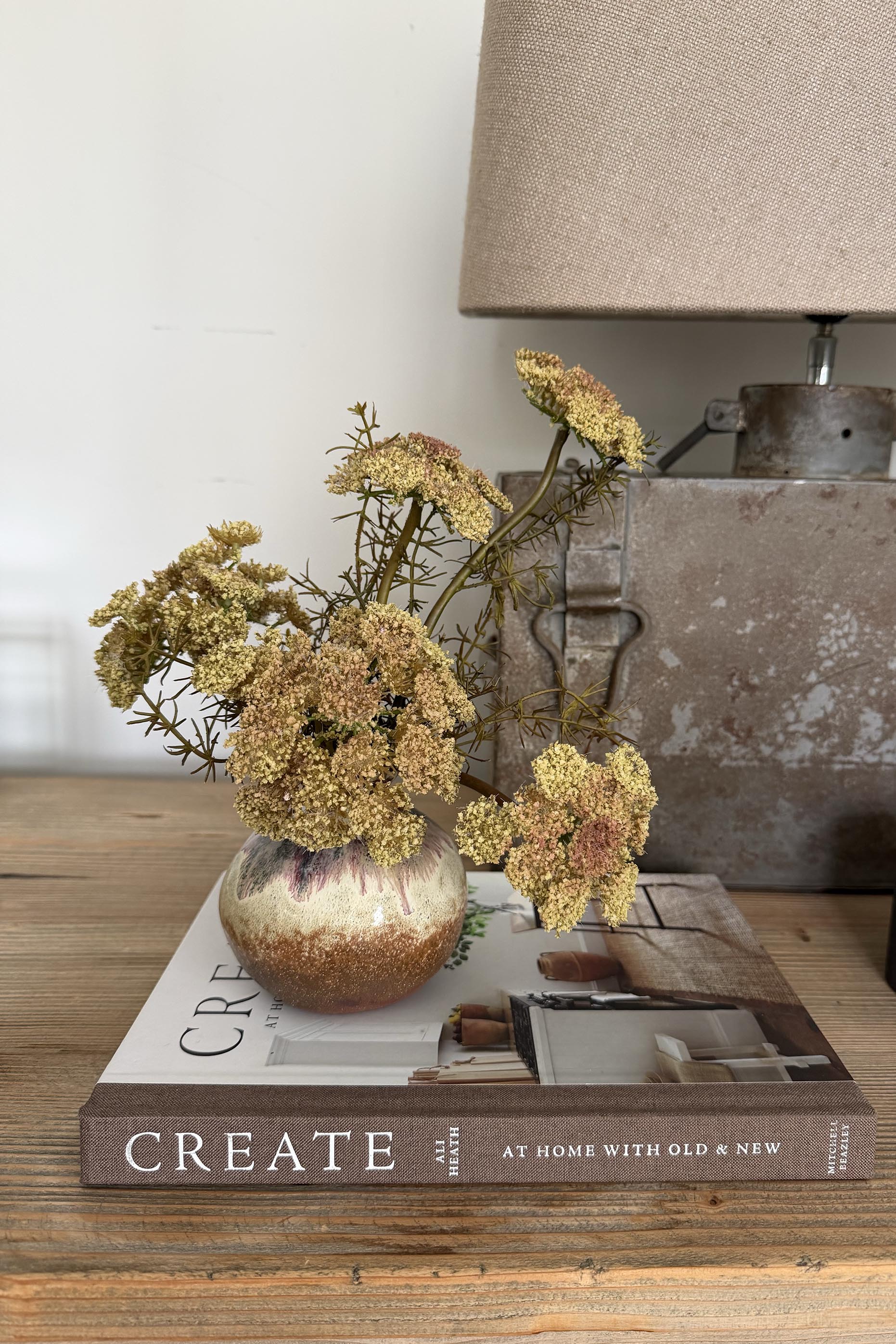 Decorative vase with flowers on a book titled 'Create' next to a lamp.