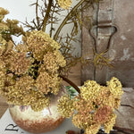 Decorative arrangement of dried flowers in a metallic vase on a textured surface.