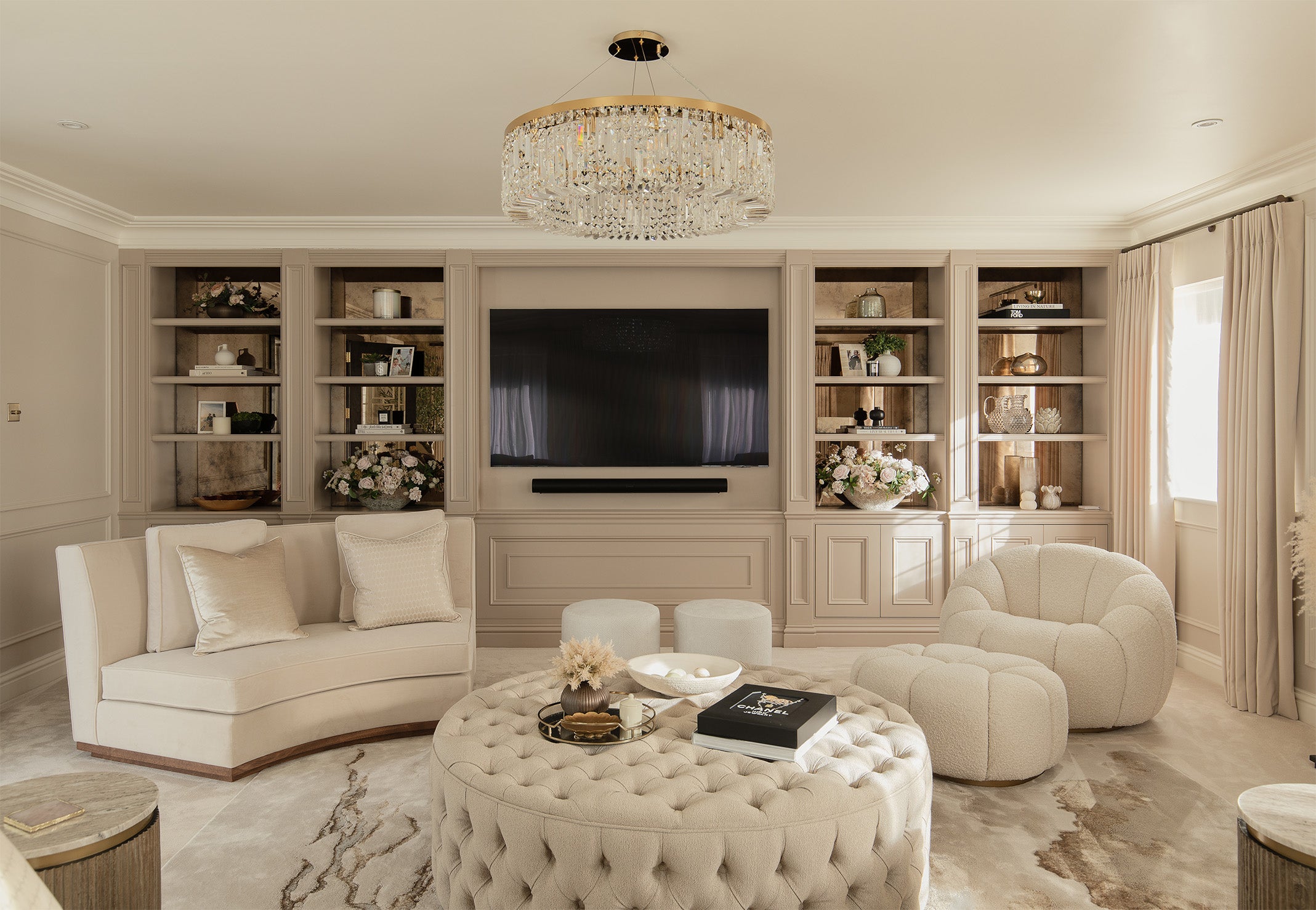 Luxurious living room with beige sofa, ottoman, and bookshelves.